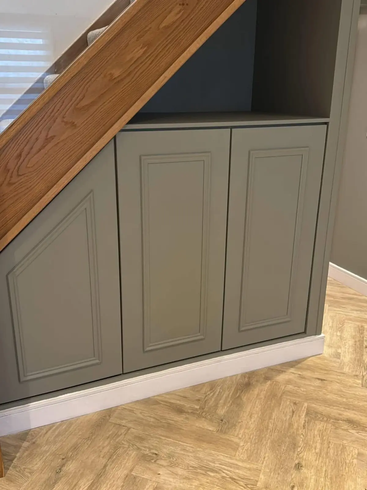 Fitted cupboards built into the space under a staircase, with panelled doors painted sage green