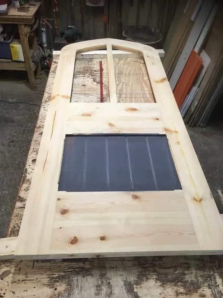 New arched door in unpainted timber in the workshop, with a dark boarded lower panel
