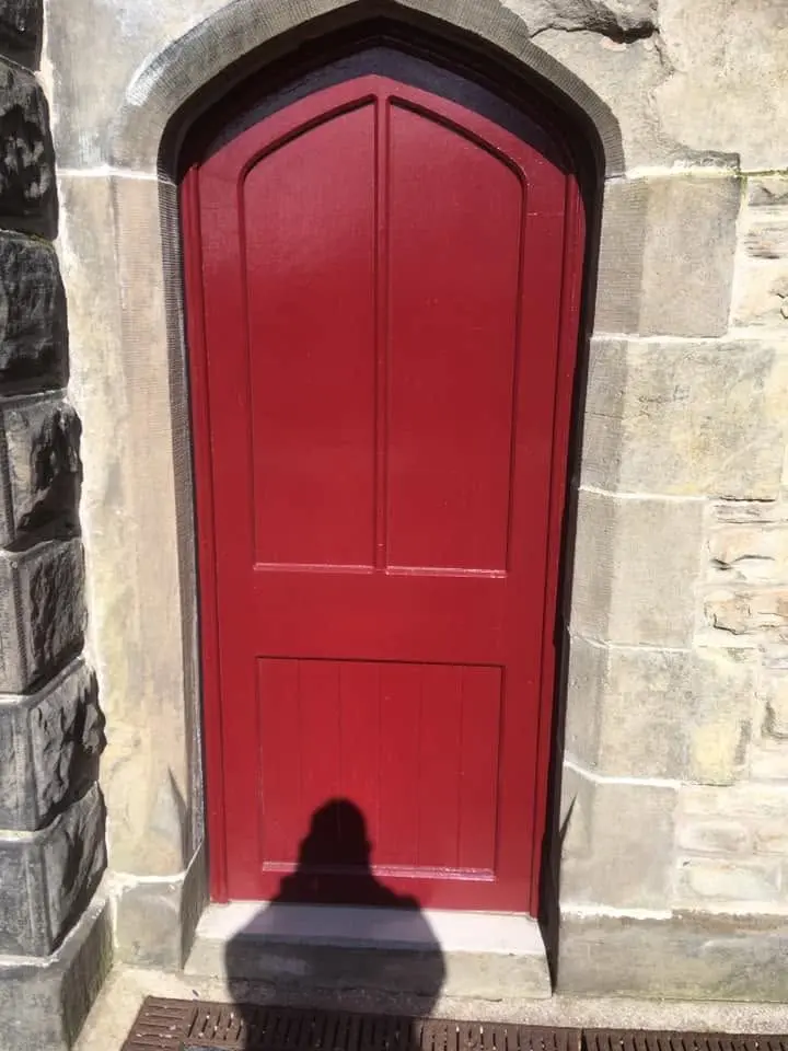 Arched door painted red, fitted in a pointed sandstone doorway