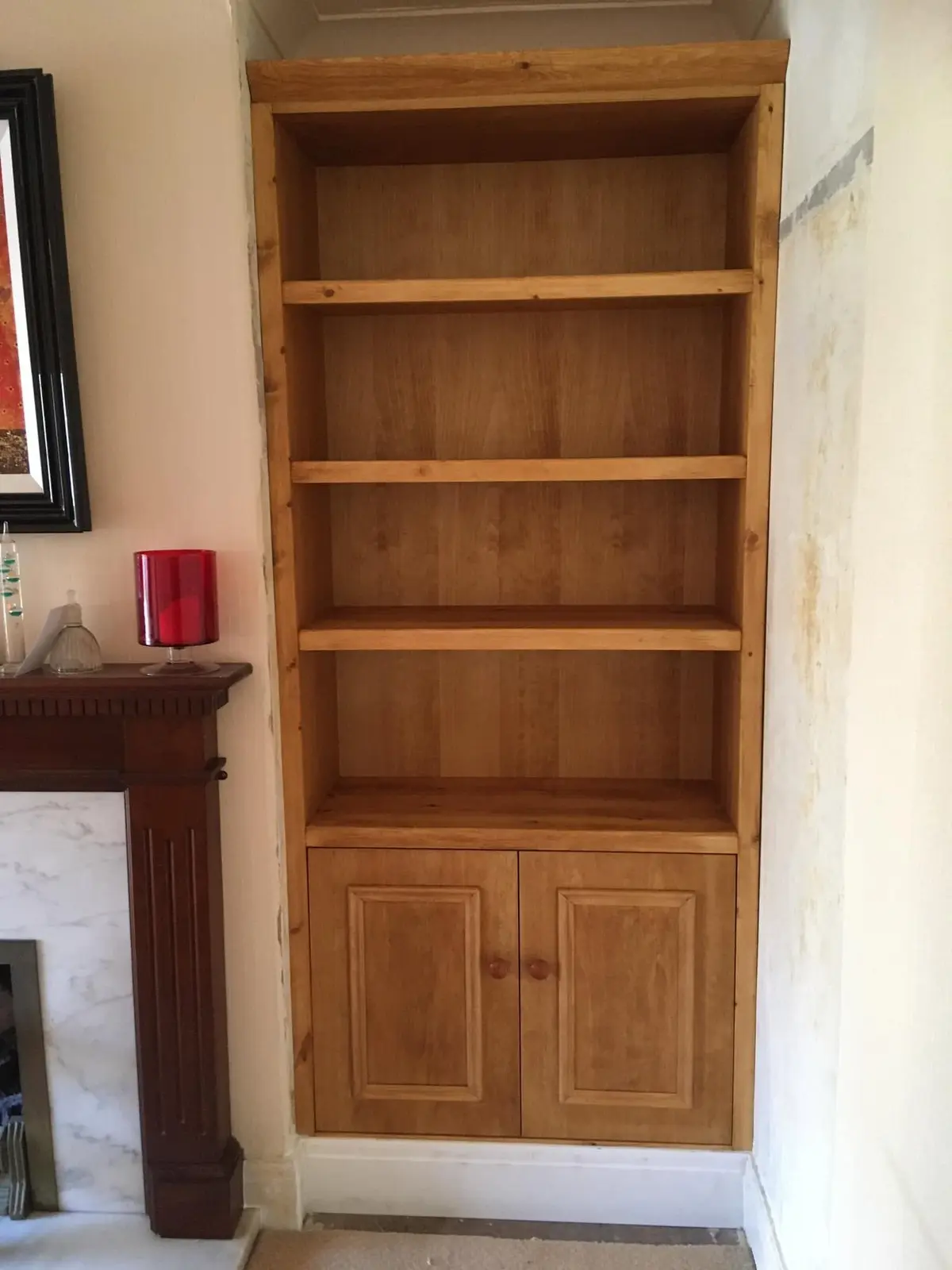 Pine bookcase with four shelves above a two-door cupboard, fitted into an alcove beside a fireplace