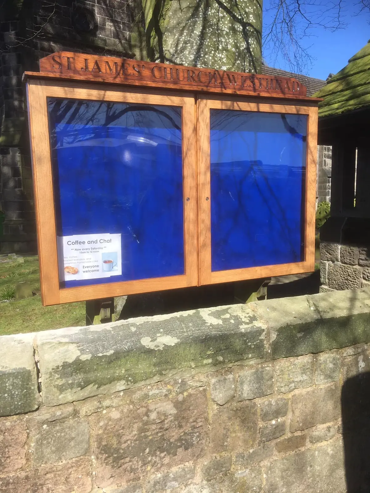 Outdoor display cabinet with two clear-fronted doors, a stained timber frame and a carved top sign